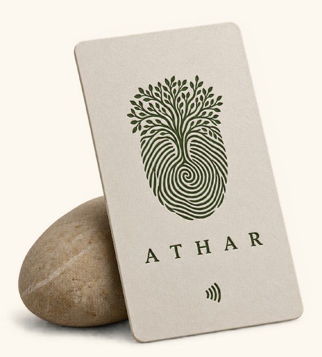 The ATHAR NFC card, cream with the mark printed in green, leaning on a smooth stone